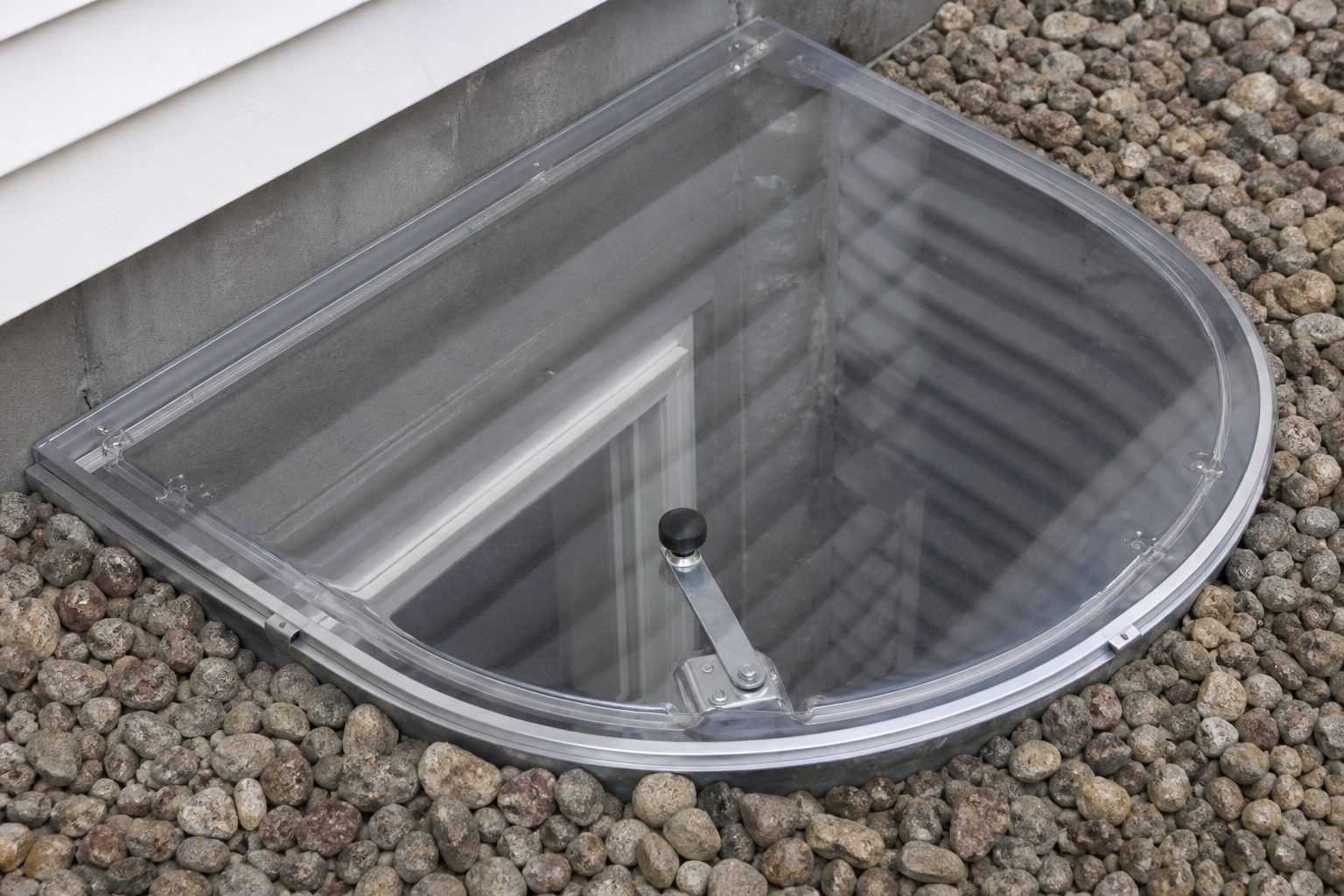 Close-up of a window well cover latch and release handle.
